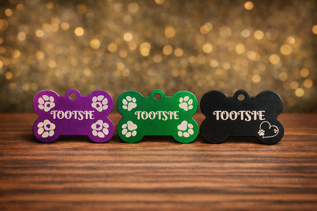 Bone Shaped Dog Tags Three bone-shaped pet tags in: purple, green and black.